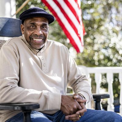 An older man sitting on a rocking chair outside on a porch