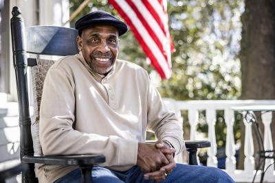 An older man sitting on a rocking chair outside on a porch