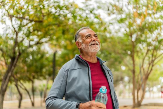A man standing outside, holding a water bottle and smiling with his chin up