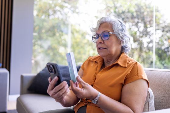 A woman holding a box of medicine to her phone while in a telehealth video call